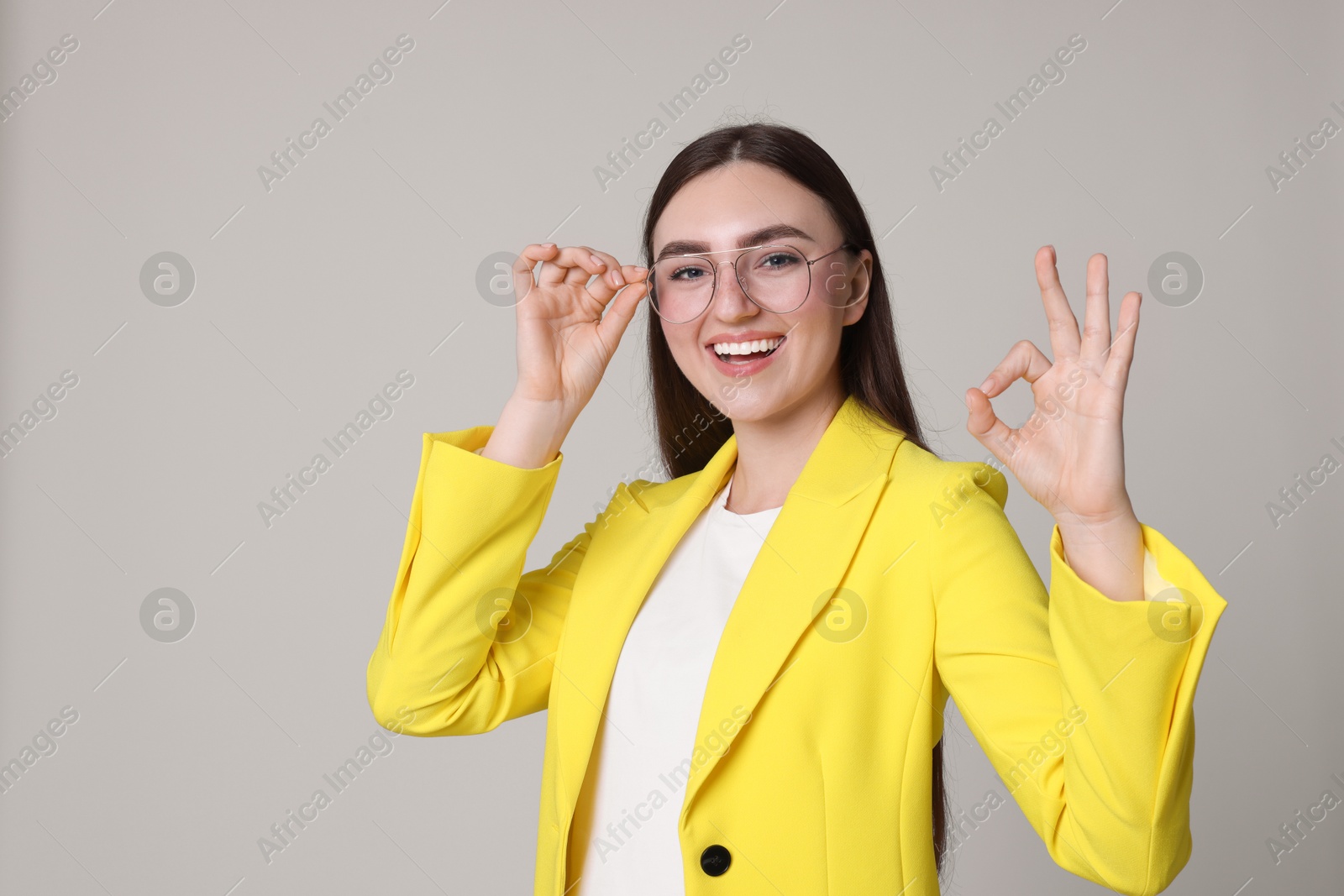 Photo of Happy young woman showing OK gesture on gray background, space for text