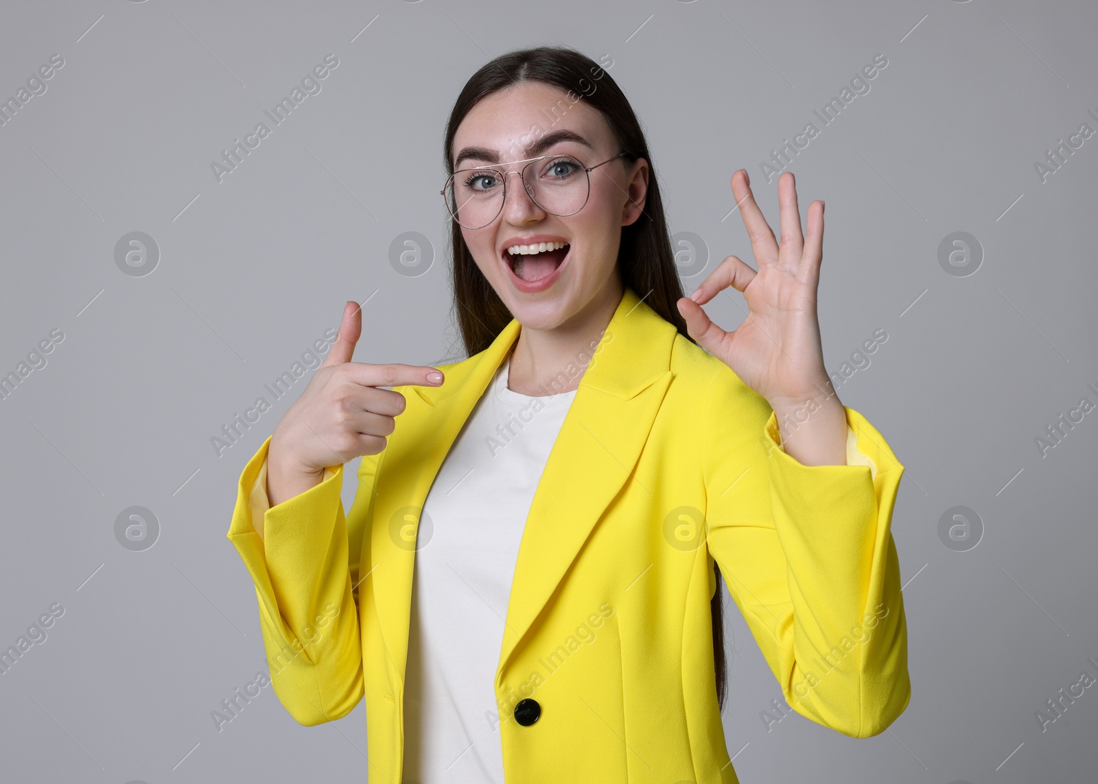 Photo of Happy young woman showing OK gesture on gray background