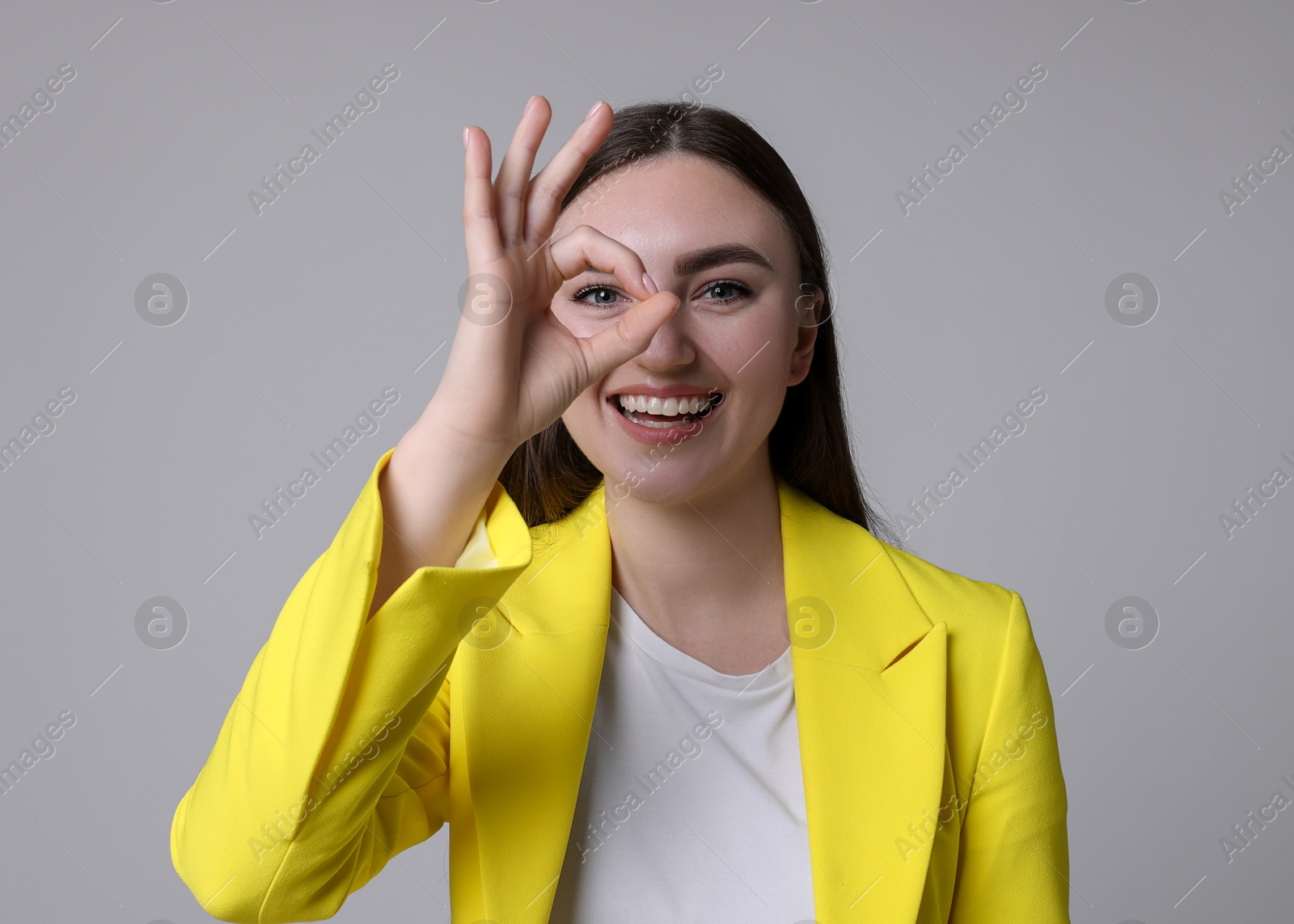 Photo of Happy young woman showing OK gesture on gray background