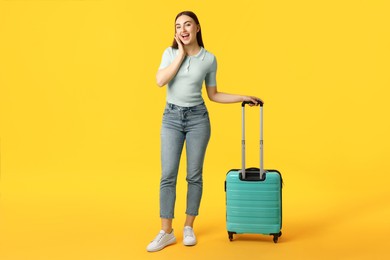 Young woman with suitcase on orange background