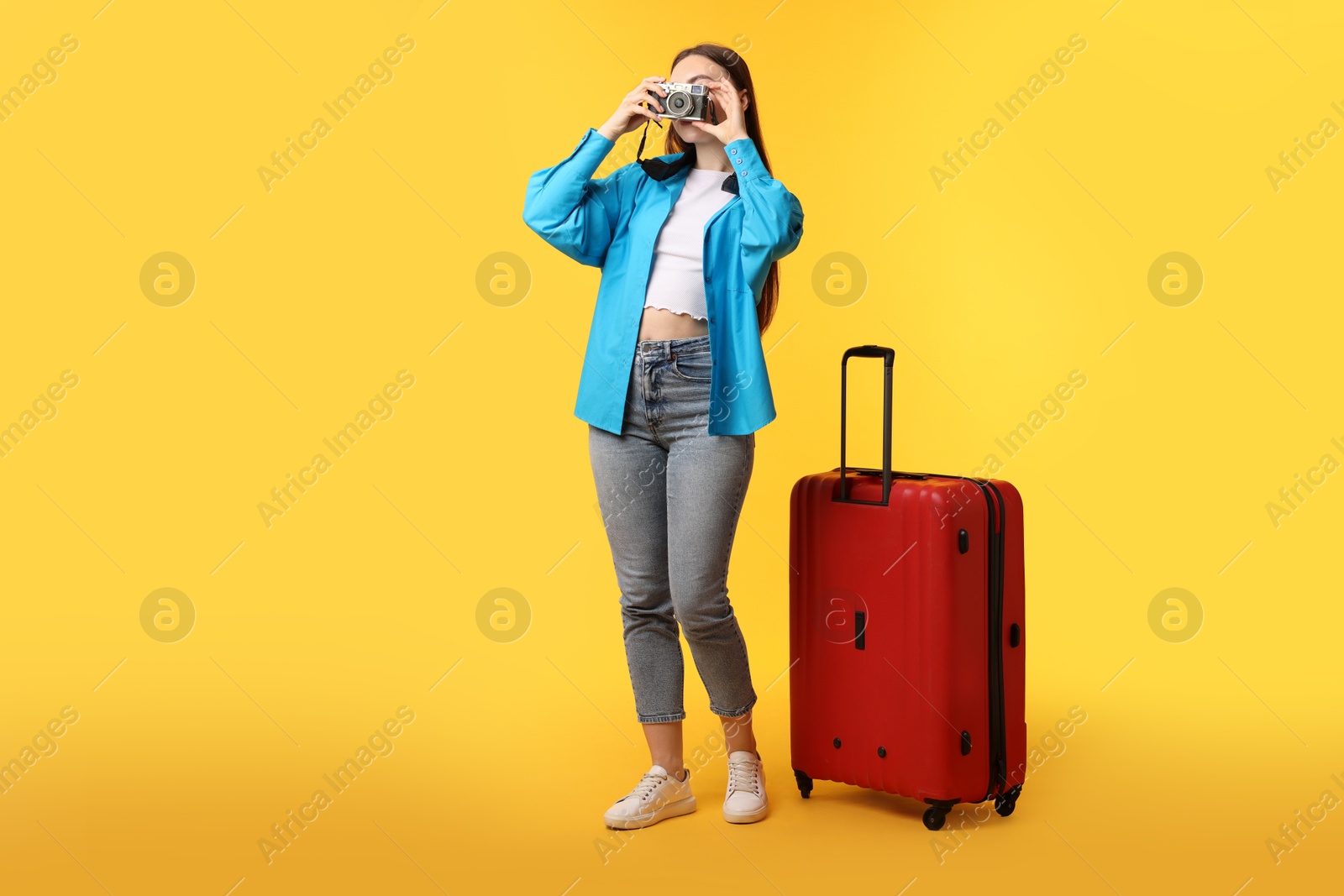 Photo of Woman with vintage camera and suitcase on orange background