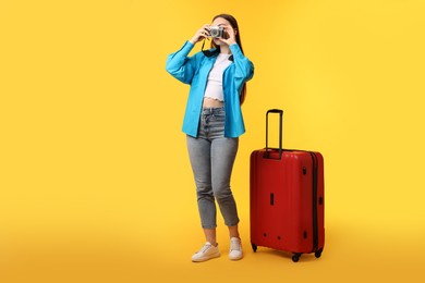 Photo of Woman with vintage camera and suitcase on orange background