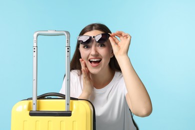 Woman with suitcase wearing sunglasses on light blue background