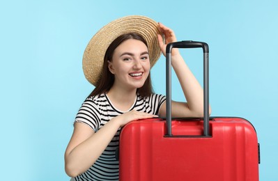 Woman in straw hat with suitcase on light blue background