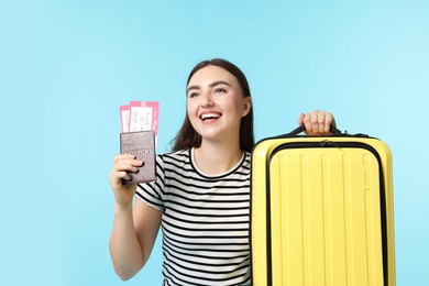 Woman with tickets, passport and suitcase on light blue background