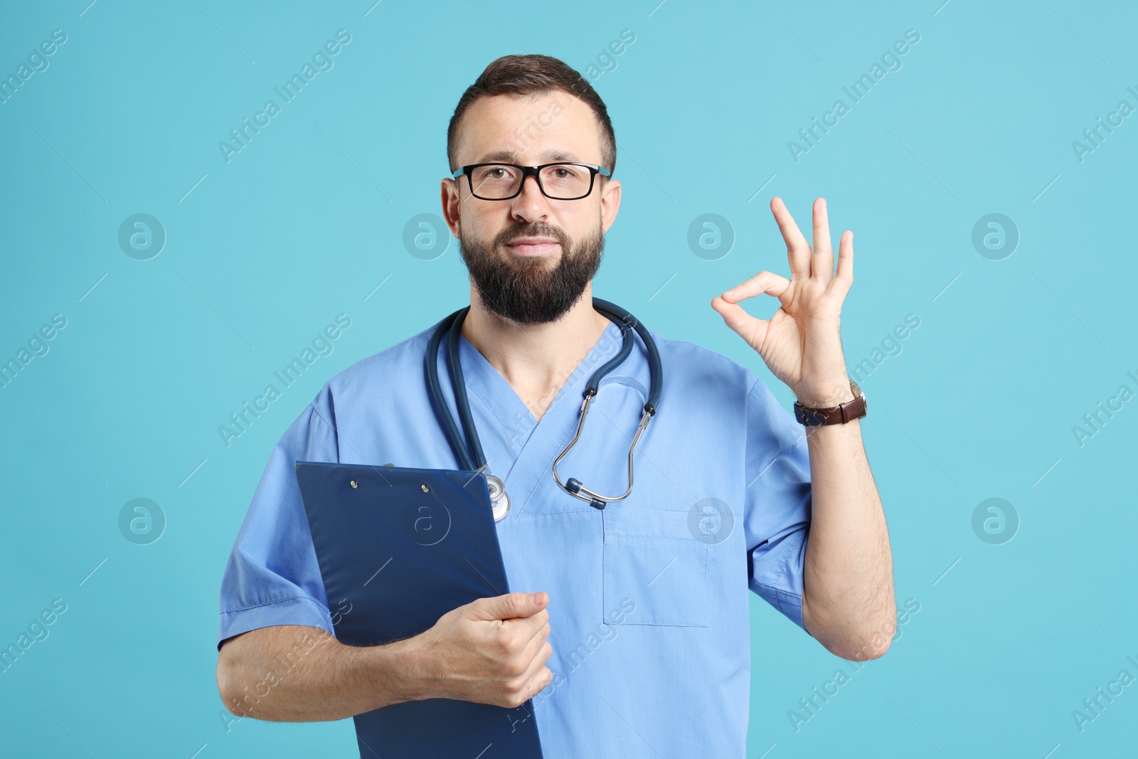 Photo of Doctor with clipboard showing okay gesture on light blue background