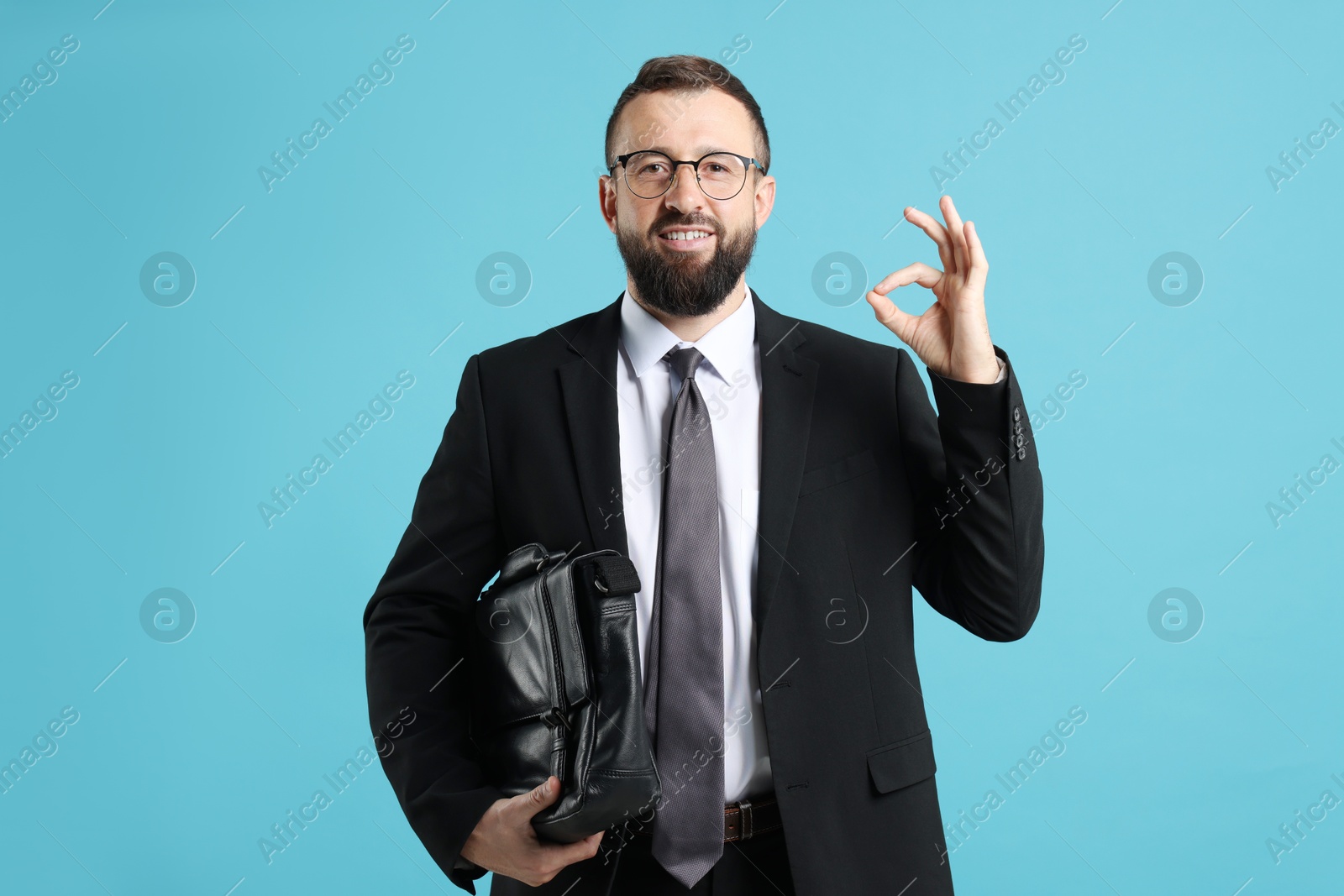 Photo of Smiling businessman showing okay gesture on light blue background