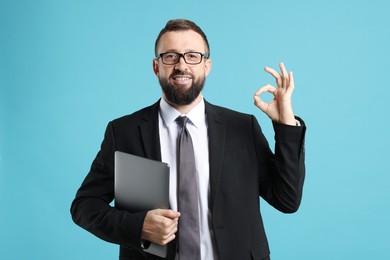 Photo of Smiling businessman with laptop showing okay gesture on light blue background