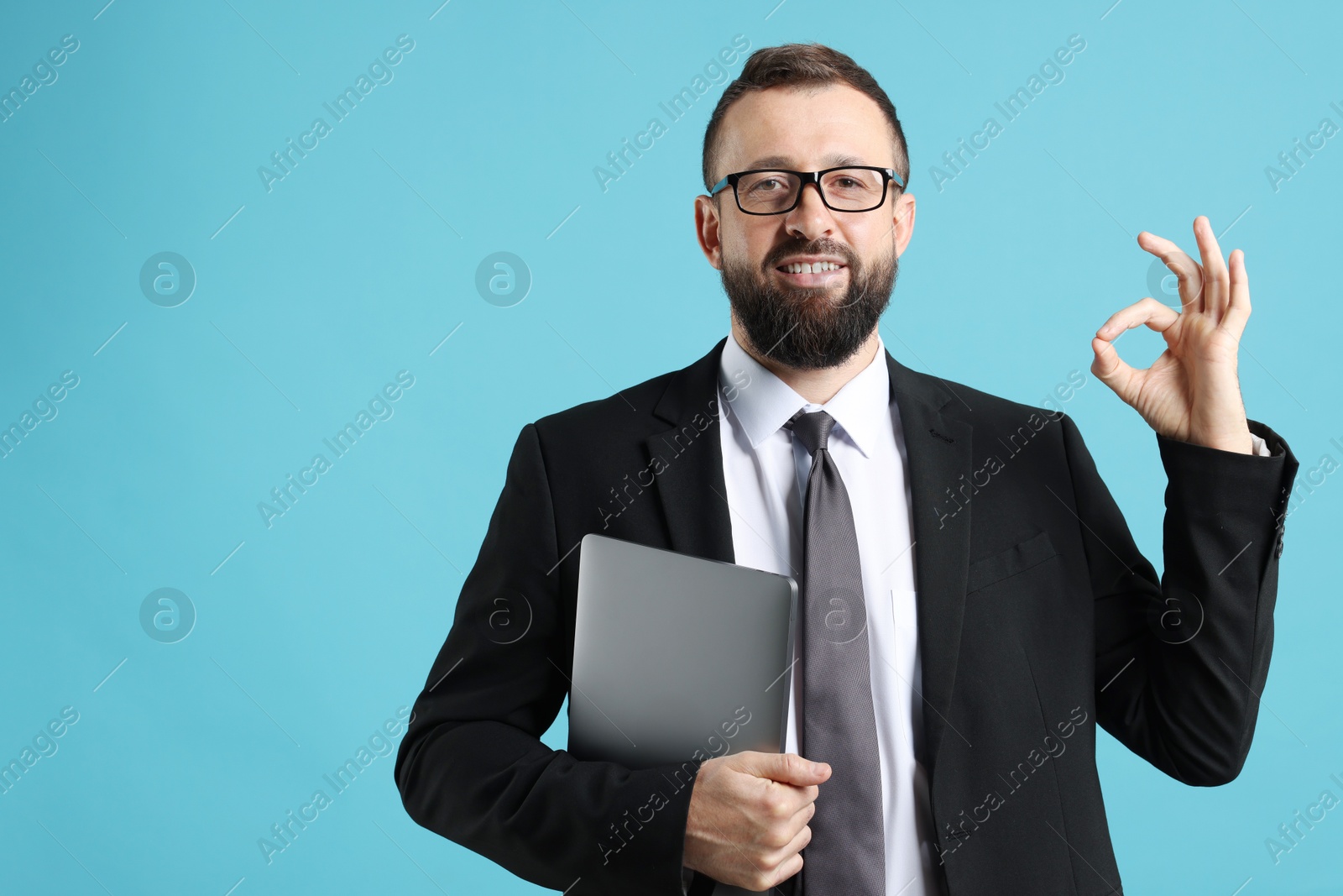 Photo of Smiling businessman with laptop showing okay gesture on light blue background. Space for text