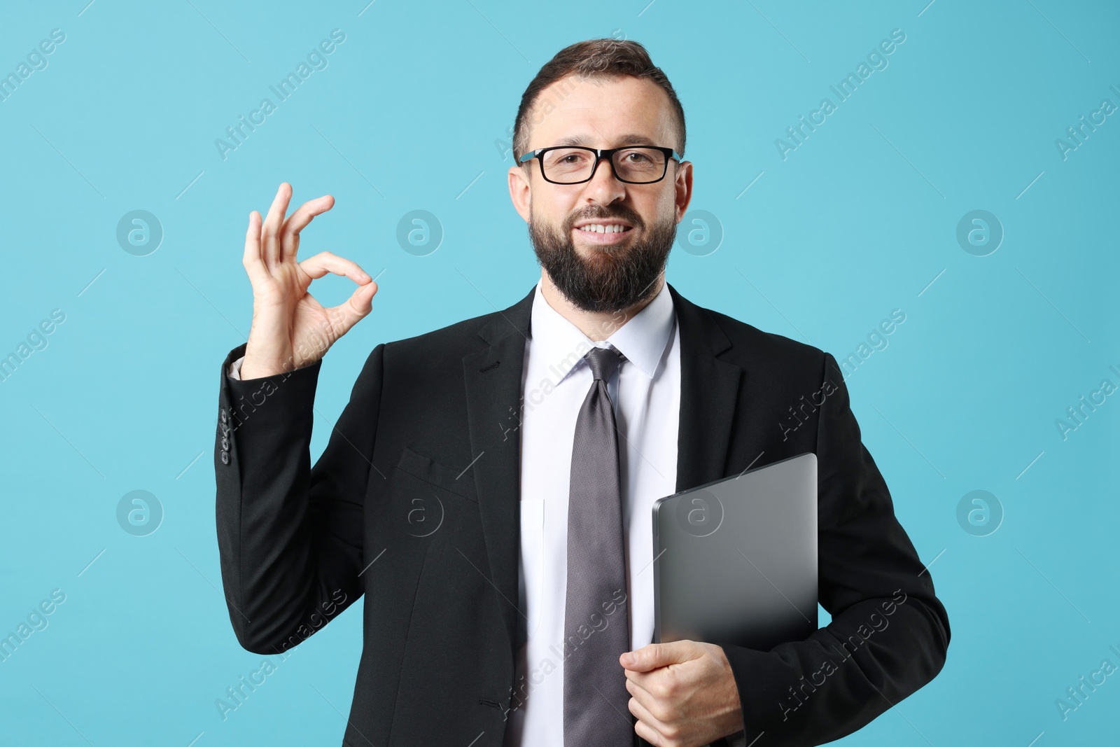 Photo of Smiling businessman with laptop showing okay gesture on light blue background