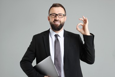 Photo of Smiling businessman with laptop showing okay gesture on grey background