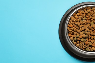 Photo of Dry pet food granules in feeding bowl on light blue background, top view. Space for text