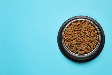 Dry pet food granules in feeding bowl on light blue background, top view. Space for text