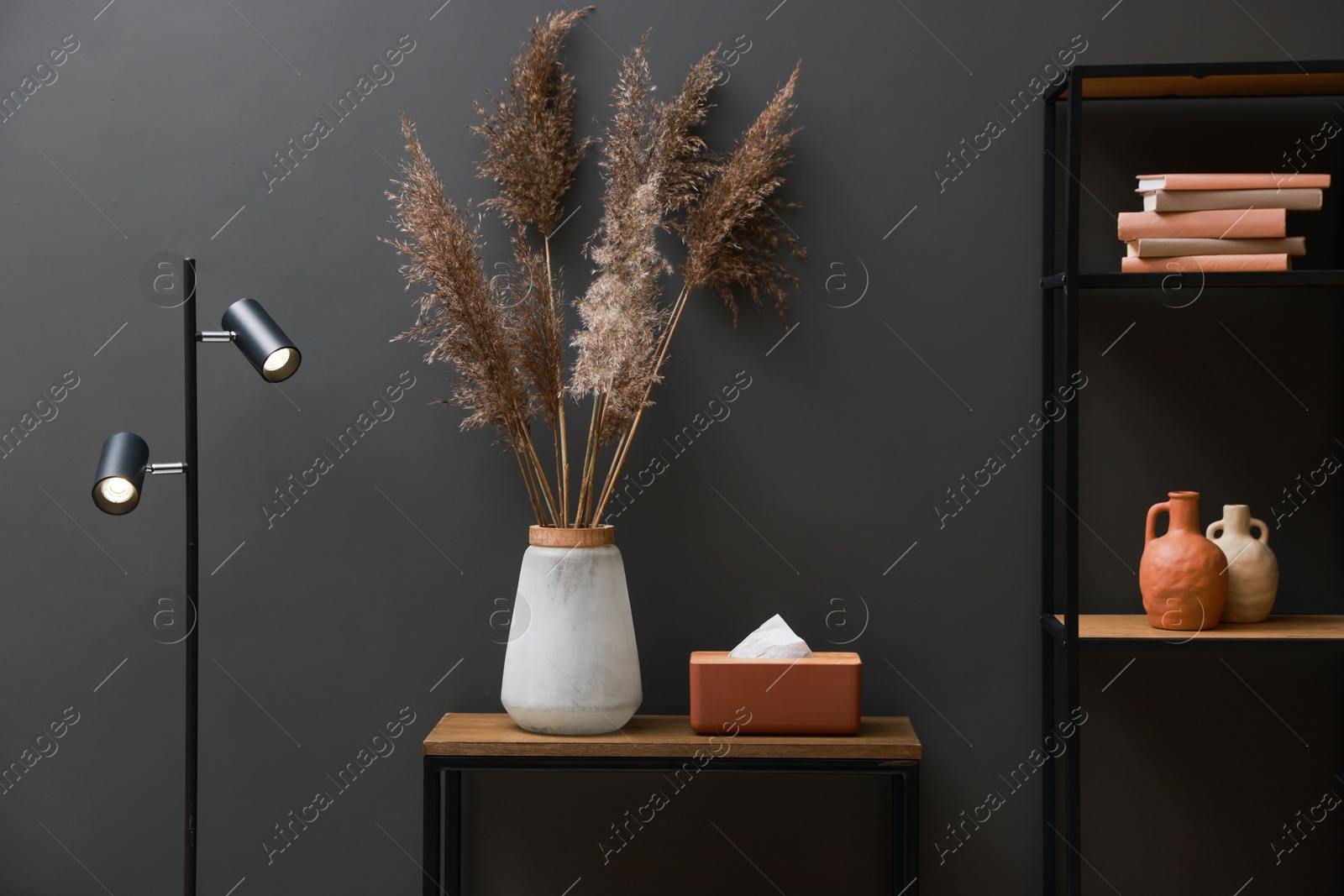 Photo of Console table with decor, lamp and shelving unit near grey wall in room. Interior design