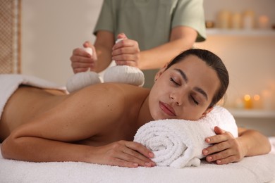 Photo of Woman receiving back massage with herbal bags in spa salon