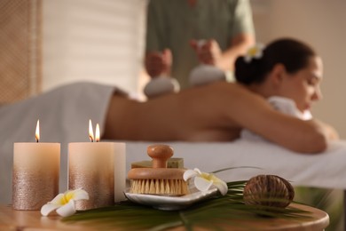 Woman receiving back massage with herbal bags in salon, focus on spa supplies