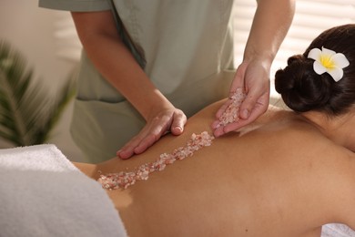 Photo of Woman receiving massage with sea salt in spa salon, closeup