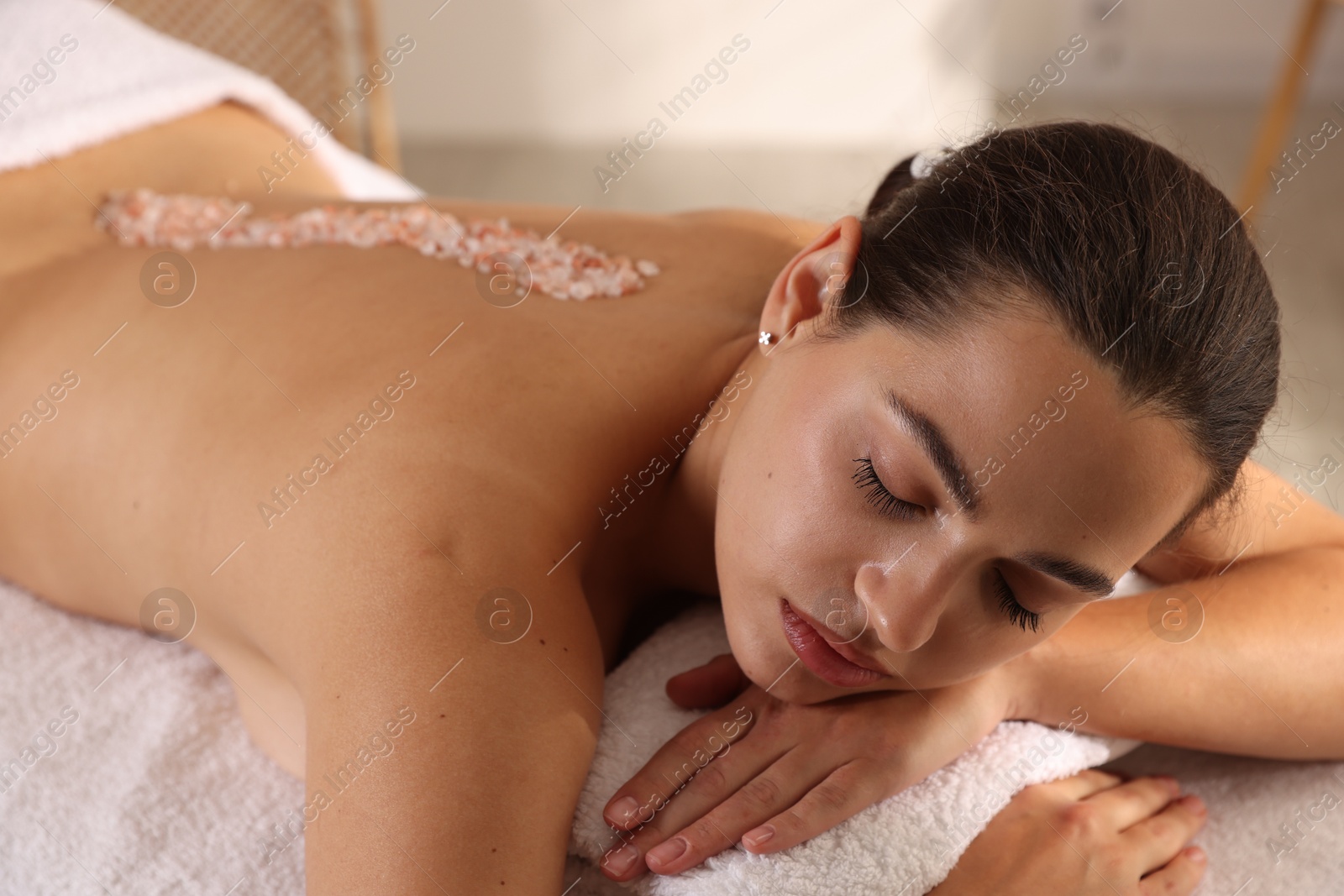 Photo of Woman with sea salt on her back lying on massage table in spa salon