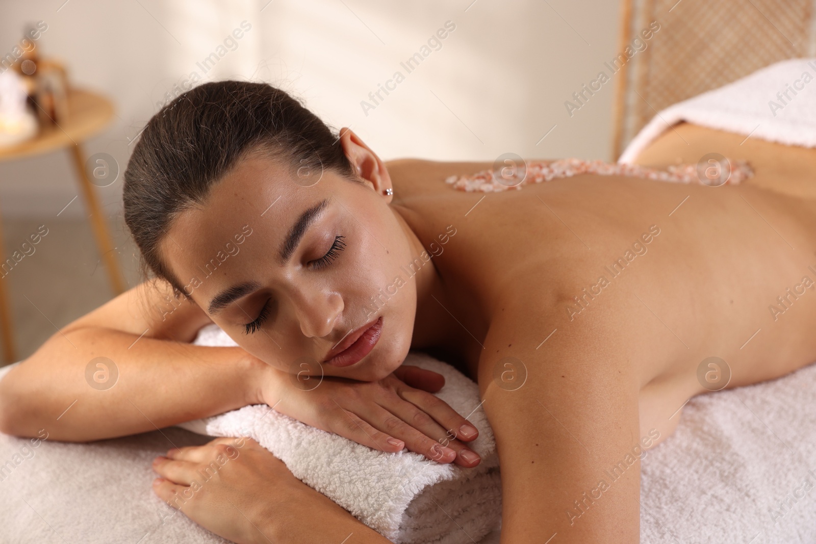 Photo of Woman with sea salt on her back lying on massage table in spa salon