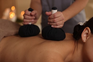 Photo of Woman receiving back massage with herbal bags in spa salon, closeup