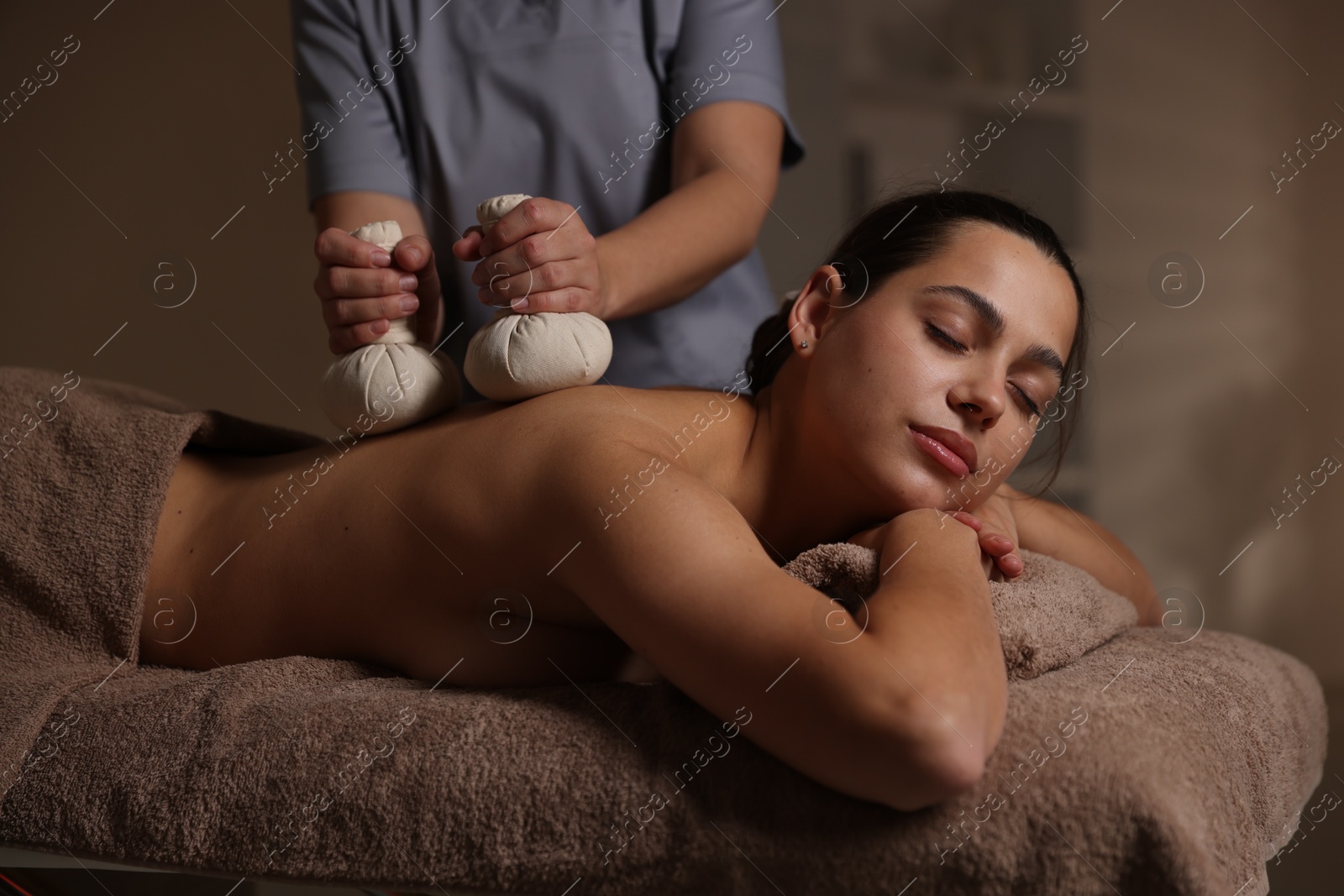 Photo of Woman receiving back massage with herbal bags in spa salon