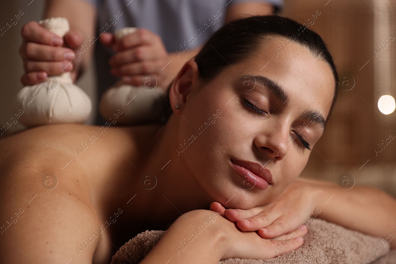 Photo of Woman receiving back massage with herbal bags in spa salon