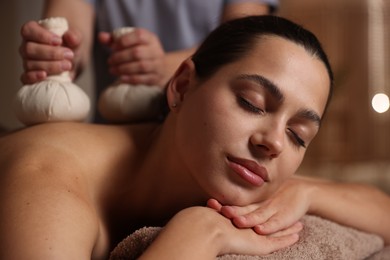 Photo of Woman receiving back massage with herbal bags in spa salon