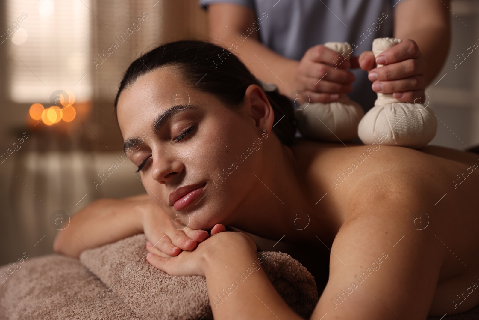 Photo of Woman receiving back massage with herbal bags in spa salon