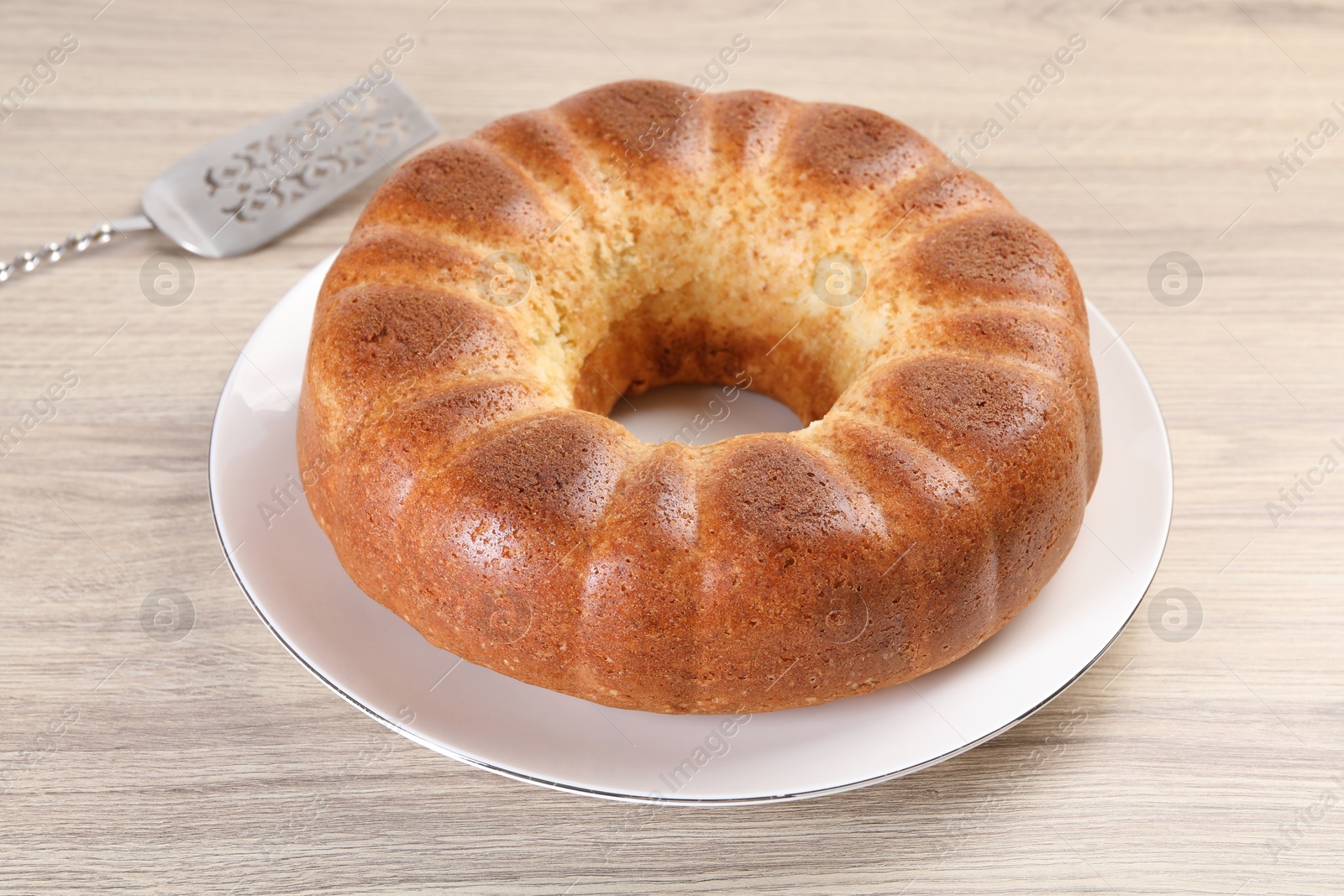 Photo of Freshly baked sponge cake and server on wooden table, closeup