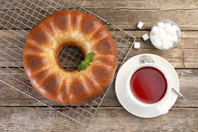 Photo of Freshly baked sponge cake, sugar cubes and tea on wooden table, top view