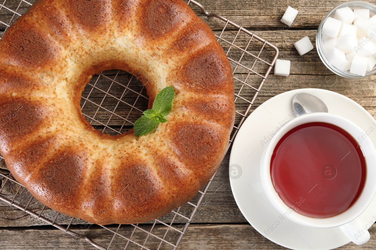 Photo of Freshly baked sponge cake, sugar cubes and tea on wooden table, top view