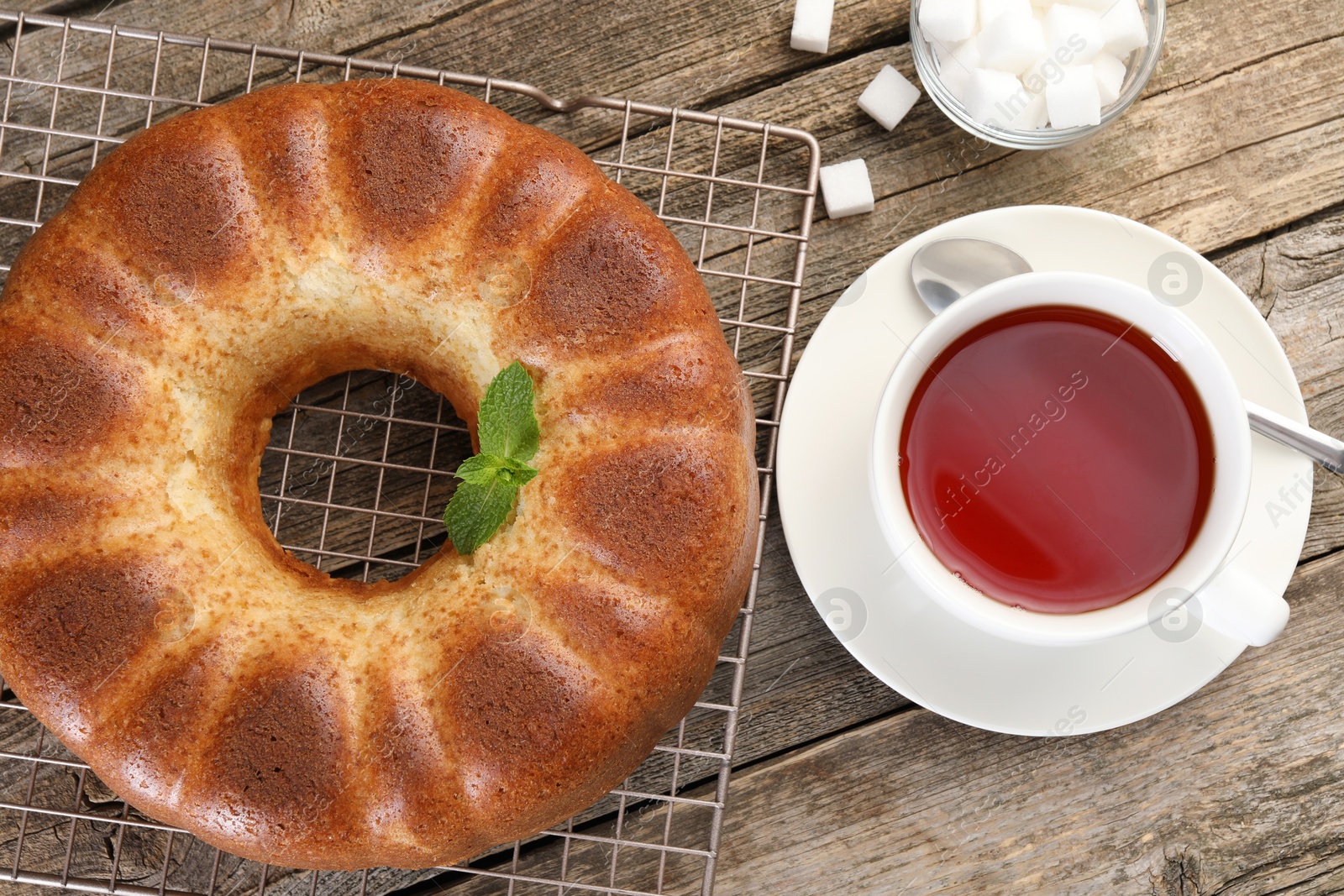 Photo of Freshly baked sponge cake, sugar cubes and tea on wooden table, top view