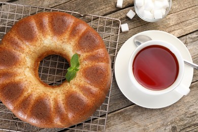 Photo of Freshly baked sponge cake, sugar cubes and tea on wooden table, top view