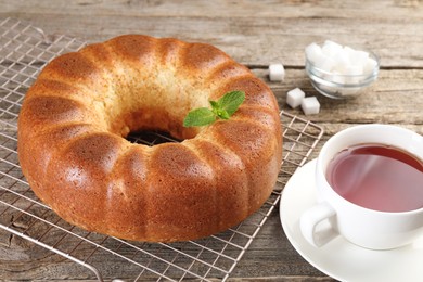 Photo of Freshly baked sponge cake, sugar cubes and tea on wooden table, closeup