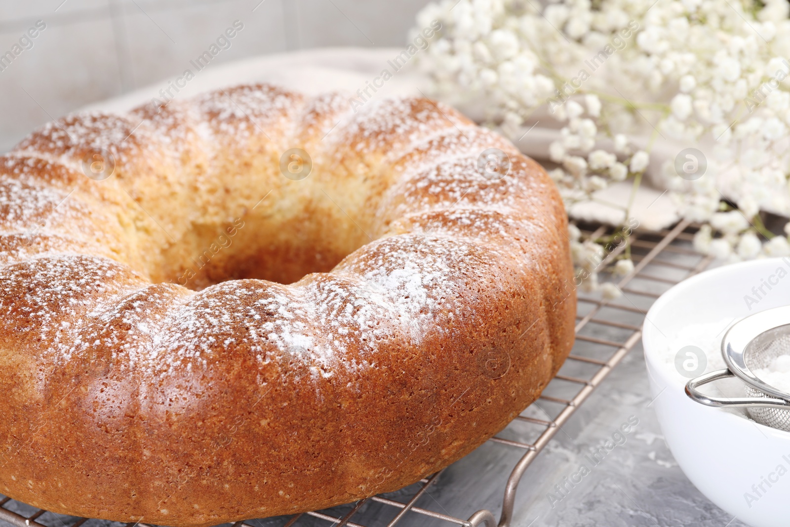 Photo of Freshly baked sponge cake with powdered sugar and flowers on grey table, closeup