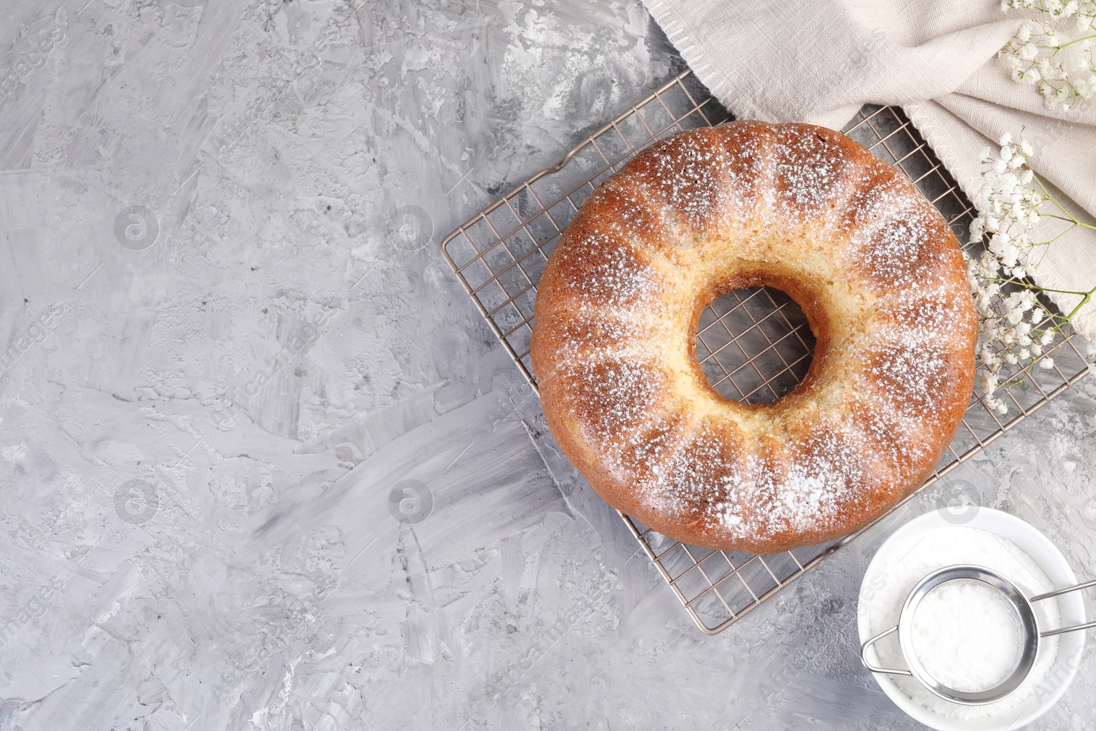 Photo of Freshly baked sponge cake with powdered sugar and flowers on grey table, top view. Space for text