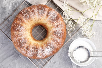 Photo of Freshly baked sponge cake with powdered sugar and flowers on grey table, top view