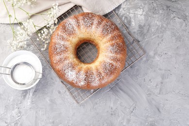 Photo of Freshly baked sponge cake with powdered sugar and flowers on grey table, top view