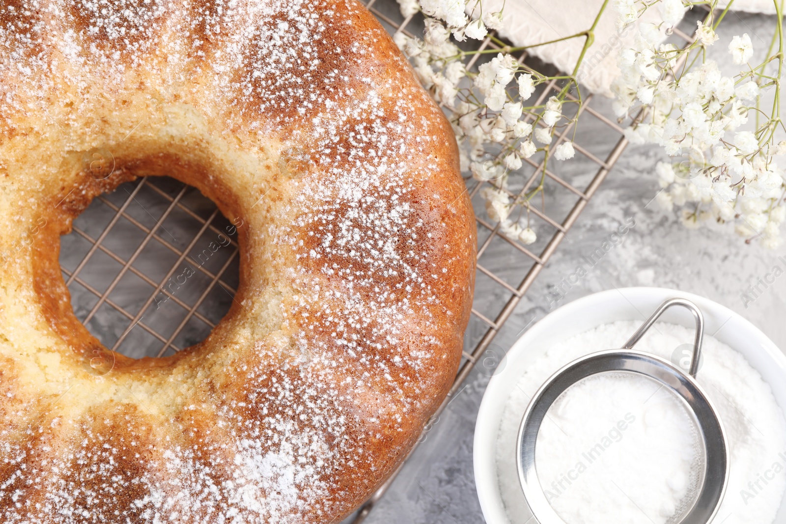 Photo of Freshly baked sponge cake with powdered sugar and flowers on grey table, top view