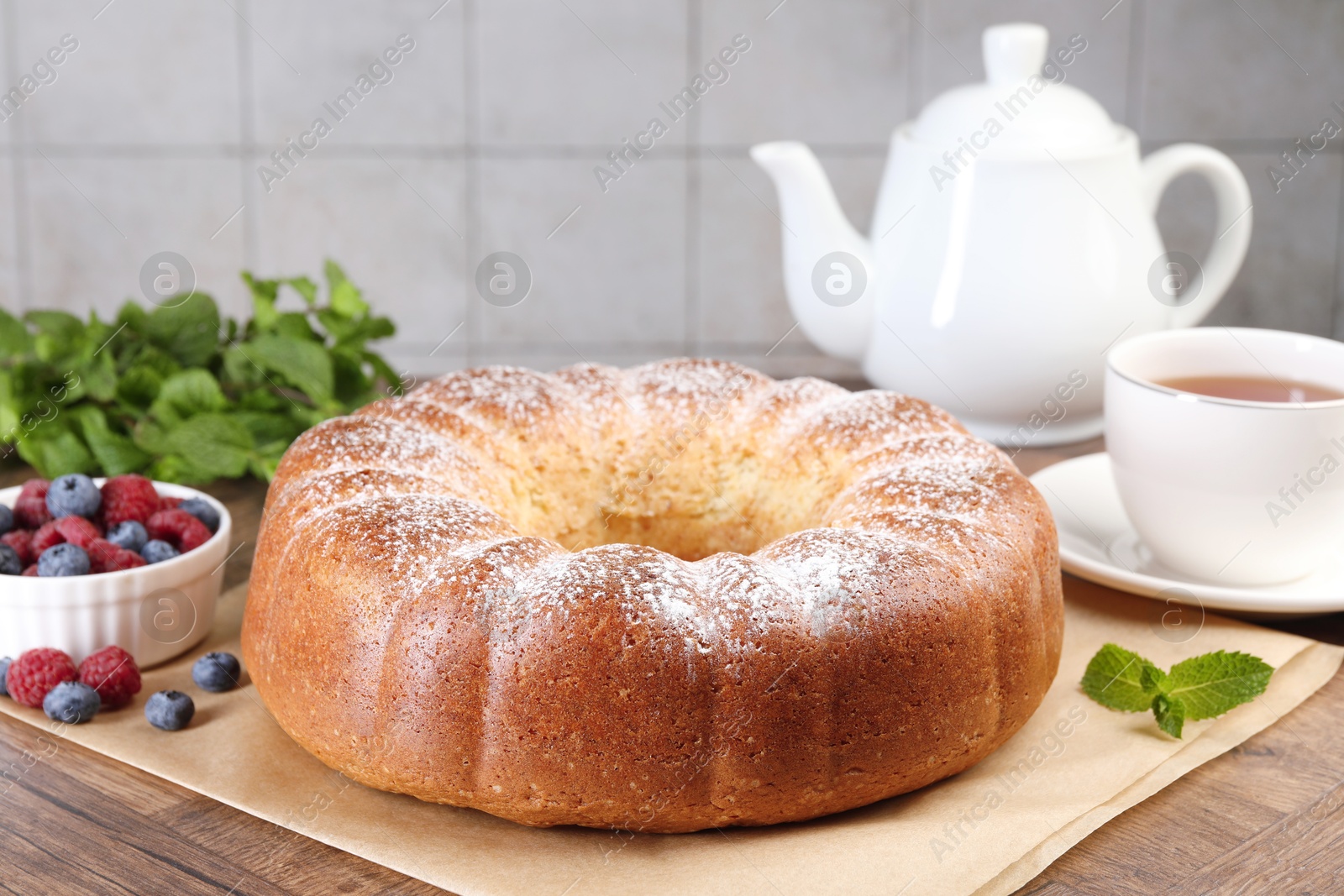 Photo of Freshly baked sponge cake, mint, berries and tea on wooden table, closeup