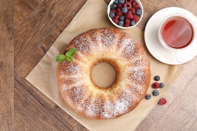 Photo of Freshly baked sponge cake, tea and berries on wooden table, top view