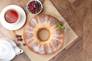 Photo of Freshly baked sponge cake, tea and berries on wooden table, top view