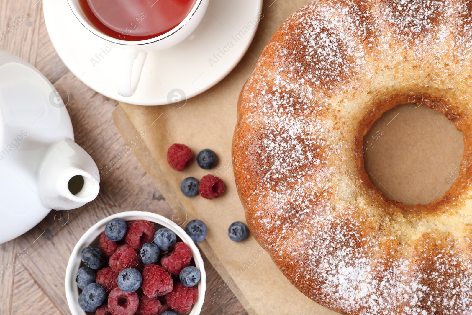 Photo of Freshly baked sponge cake, tea and berries on wooden table, top view