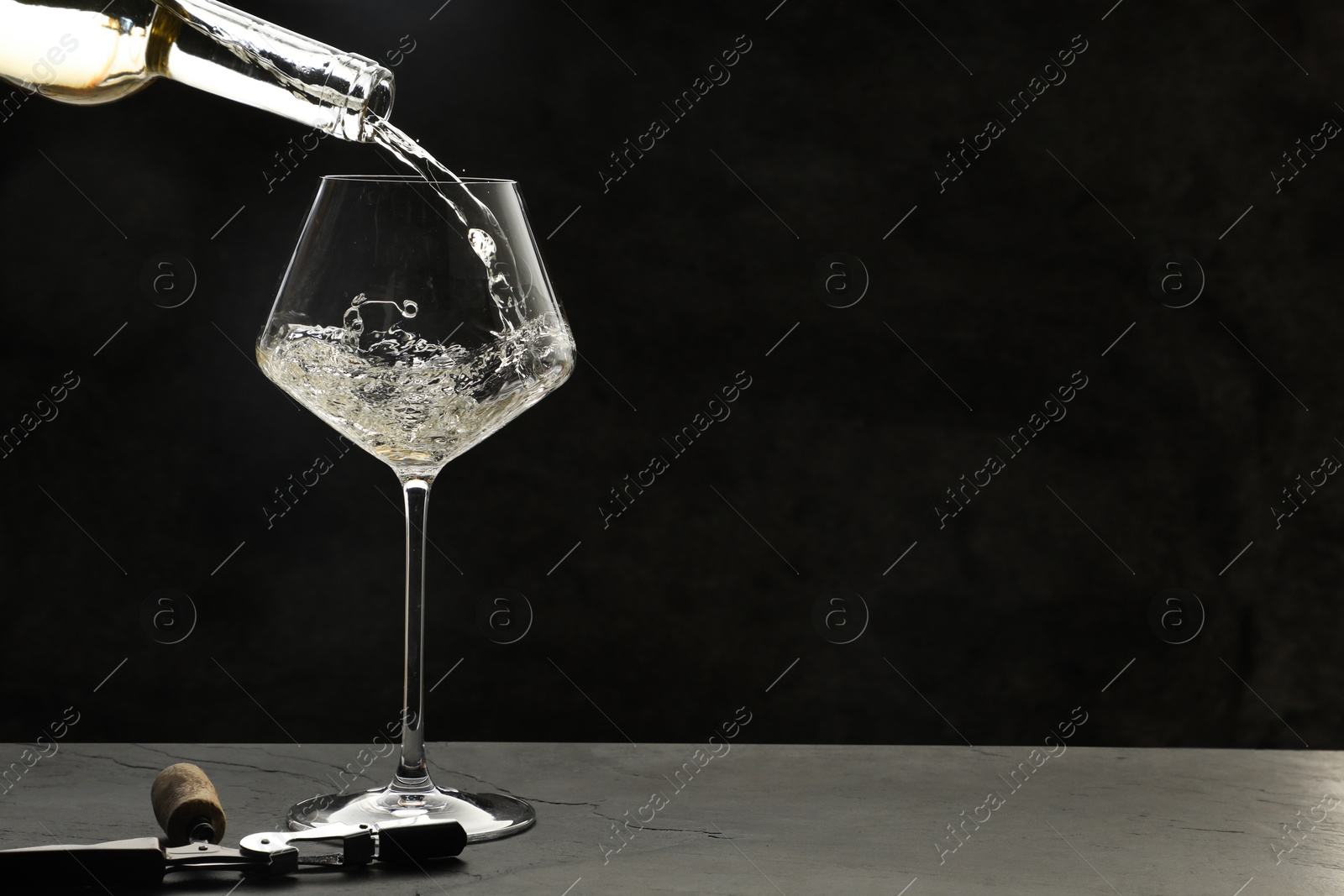 Photo of Pouring white wine into glass at grey table, space for text