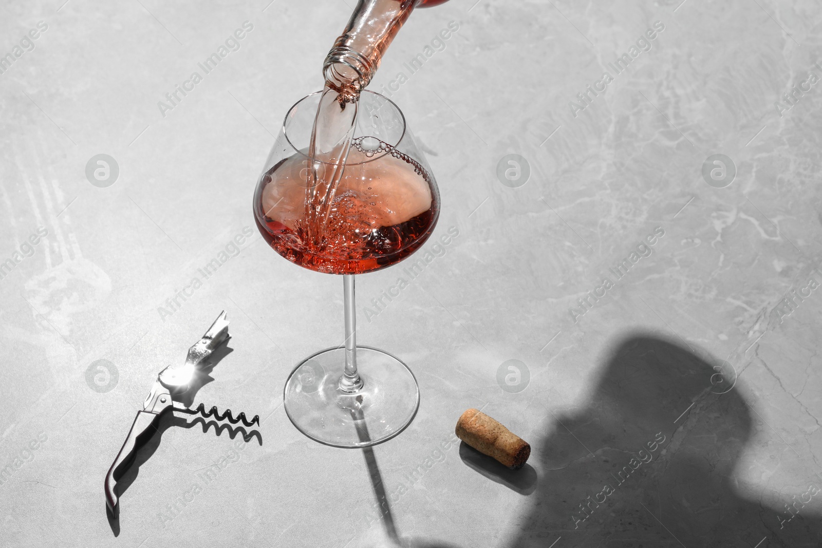 Photo of Pouring rose wine into glass at grey marble table