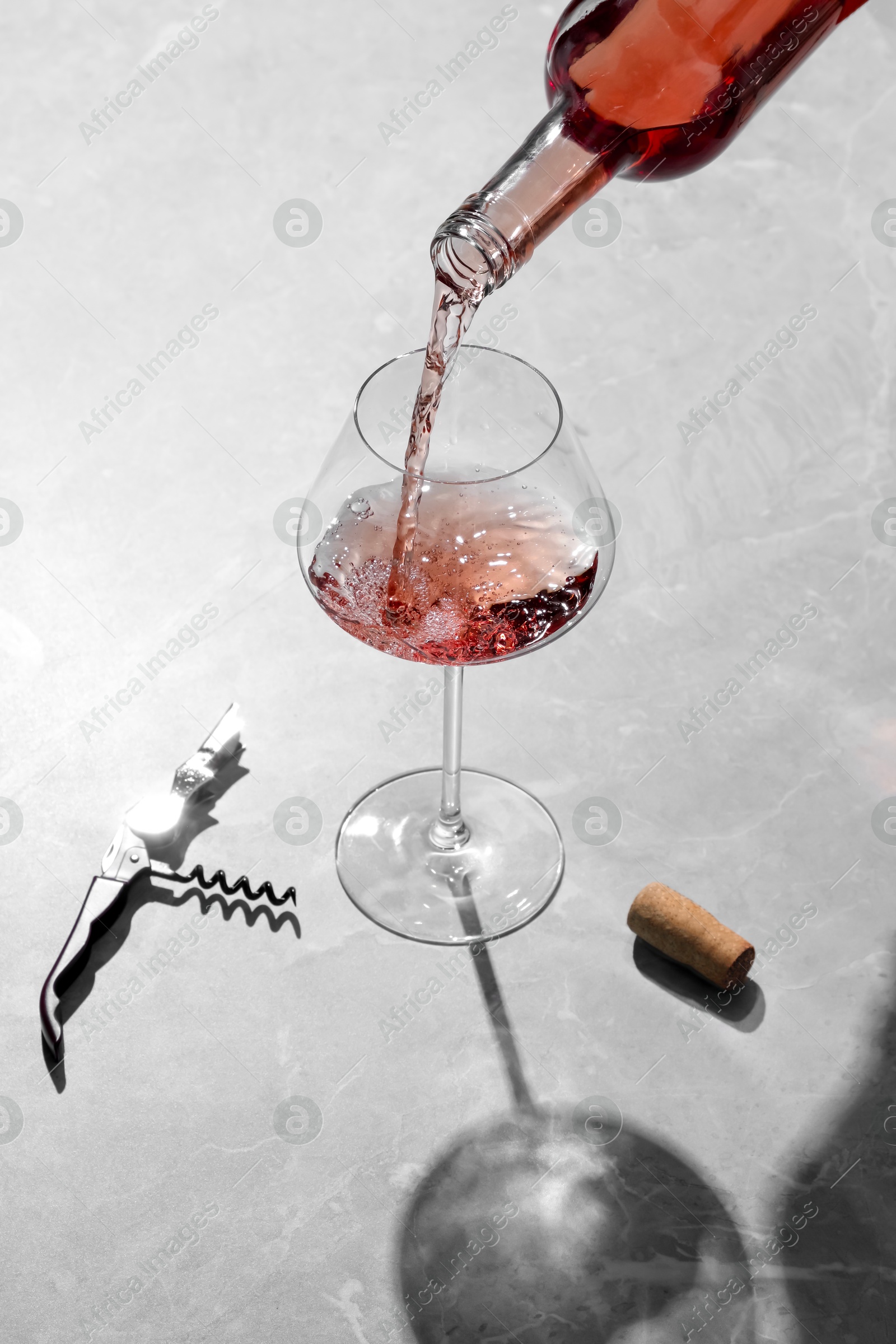 Photo of Pouring rose wine into glass at grey marble table