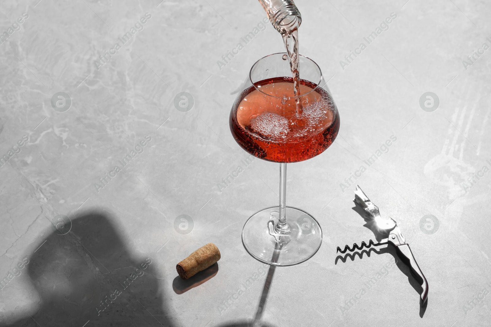 Photo of Pouring rose wine into glass at grey marble table