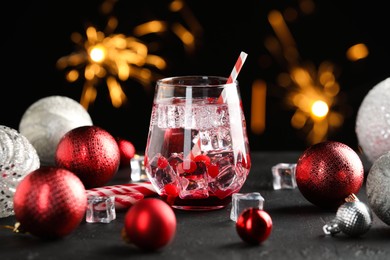 Photo of Tasty Christmas cocktail in glass, ice cubes and decor on black table against blurred lights, closeup