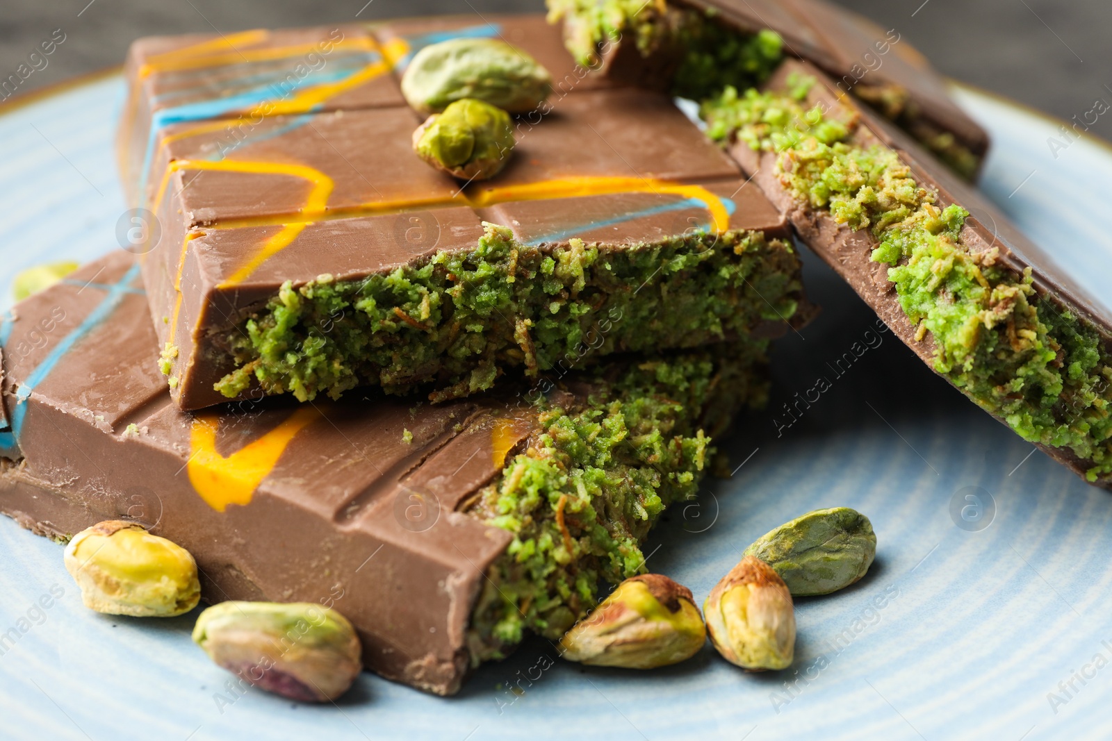 Photo of Pieces of Dubai chocolate bar with pistachios and knafeh on plate, closeup