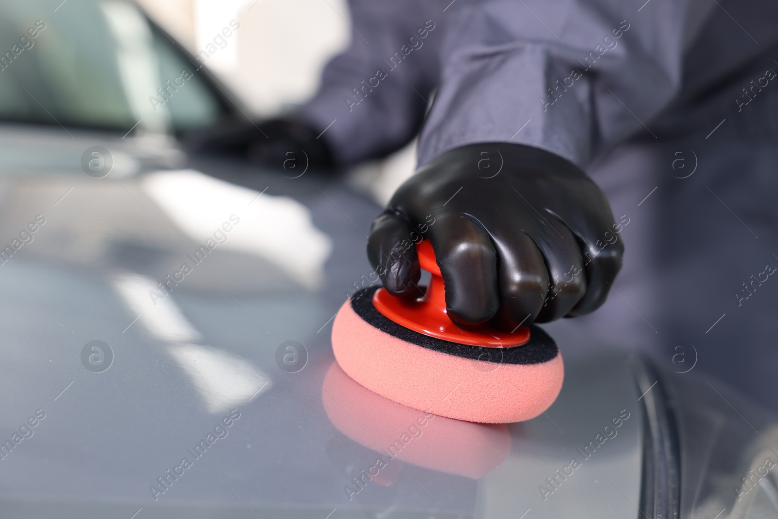 Photo of Man polishing car hood with sponge indoors, closeup